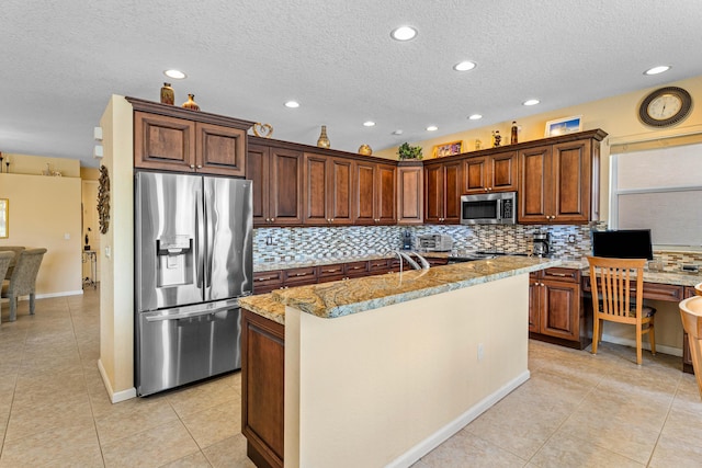 kitchen with stainless steel appliances, tasteful backsplash, a kitchen island with sink, and light stone counters