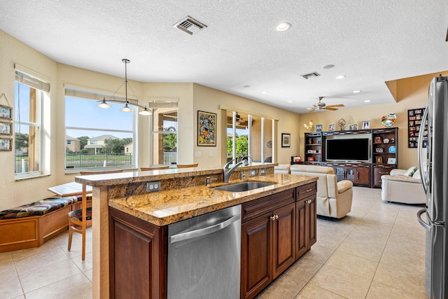 kitchen with sink, hanging light fixtures, a center island with sink, appliances with stainless steel finishes, and light stone countertops