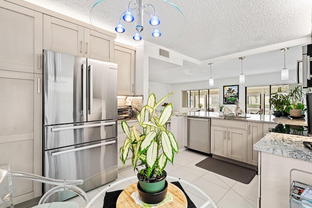 kitchen with light tile patterned floors, appliances with stainless steel finishes, tasteful backsplash, light stone countertops, and a textured ceiling