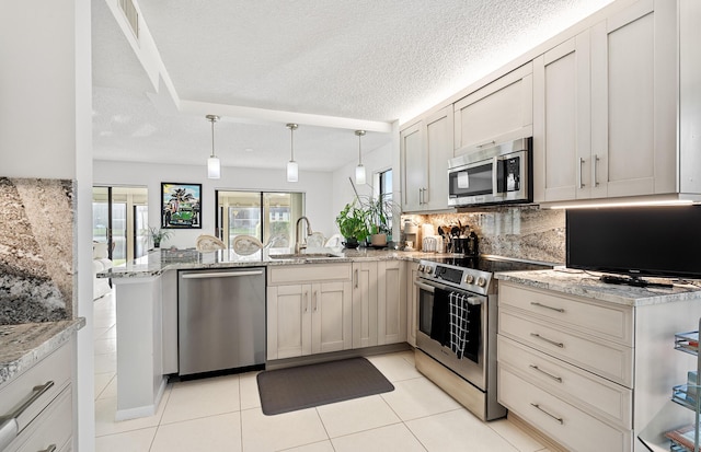 kitchen with appliances with stainless steel finishes, pendant lighting, light stone counters, and kitchen peninsula