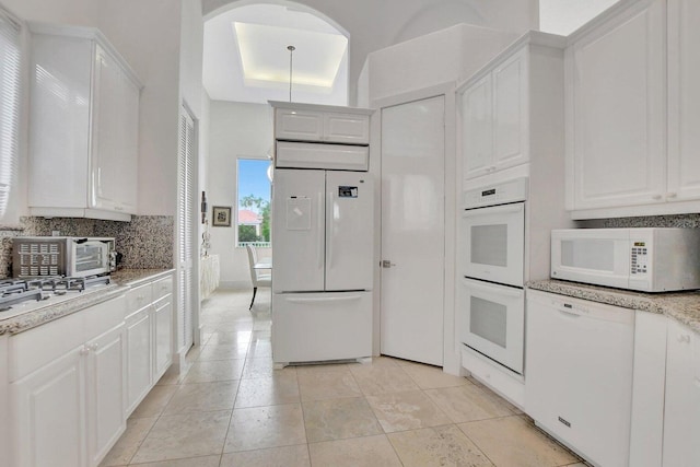 kitchen with white appliances, white cabinetry, tasteful backsplash, a tray ceiling, and light tile patterned flooring