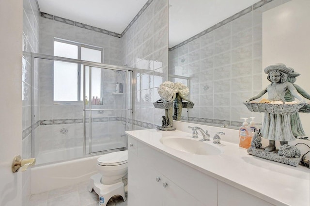 full bathroom with combined bath / shower with glass door, tile walls, tile patterned flooring, vanity, and toilet