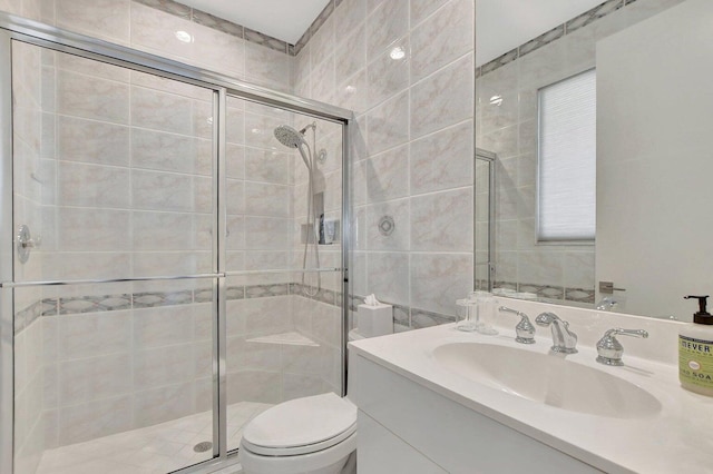 bathroom featuring vanity, a shower with shower door, tile walls, and toilet