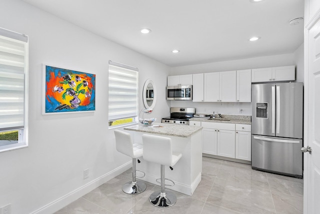 kitchen featuring appliances with stainless steel finishes, white cabinetry, a breakfast bar area, a center island, and light stone countertops