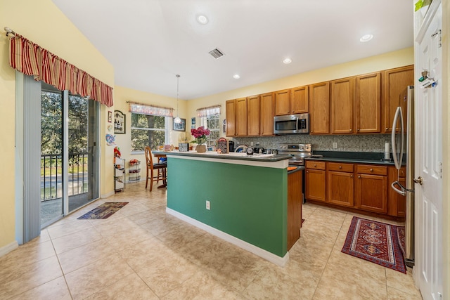 kitchen featuring light tile patterned floors, appliances with stainless steel finishes, tasteful backsplash, an island with sink, and decorative light fixtures