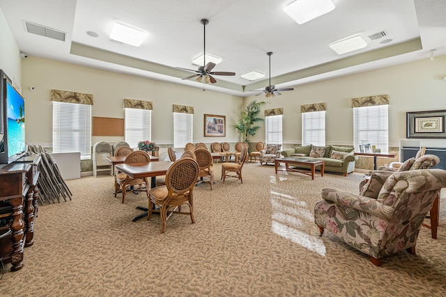 carpeted living room with ceiling fan and a raised ceiling