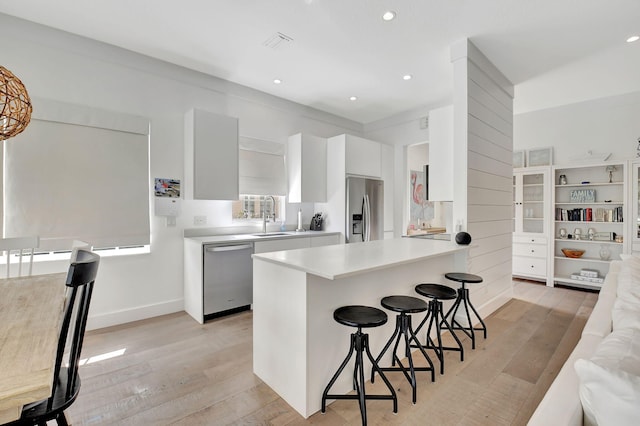 kitchen with a breakfast bar, sink, white cabinets, stainless steel appliances, and light wood-type flooring