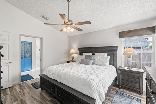 bedroom with ceiling fan, a textured ceiling, vaulted ceiling, and wood-type flooring