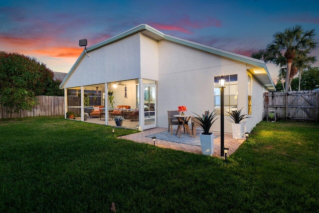 back house at dusk featuring a yard, a sunroom, and a patio area