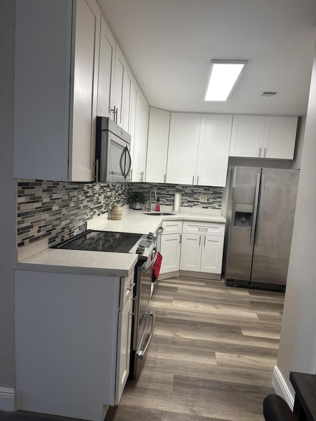 kitchen featuring sink, stainless steel appliances, light hardwood / wood-style floors, decorative backsplash, and white cabinets