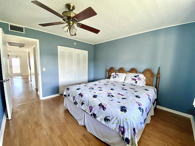 bedroom with a textured ceiling, light wood-type flooring, ornamental molding, a closet, and ceiling fan