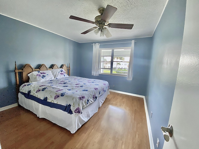 bedroom with ceiling fan, crown molding, wood-type flooring, and a textured ceiling