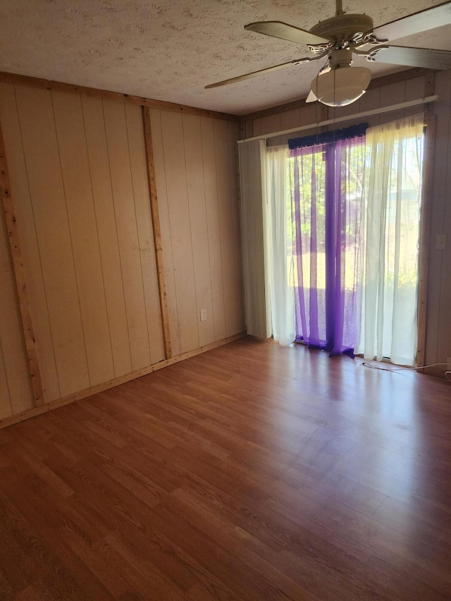 unfurnished room with ceiling fan, hardwood / wood-style floors, a textured ceiling, and wood walls