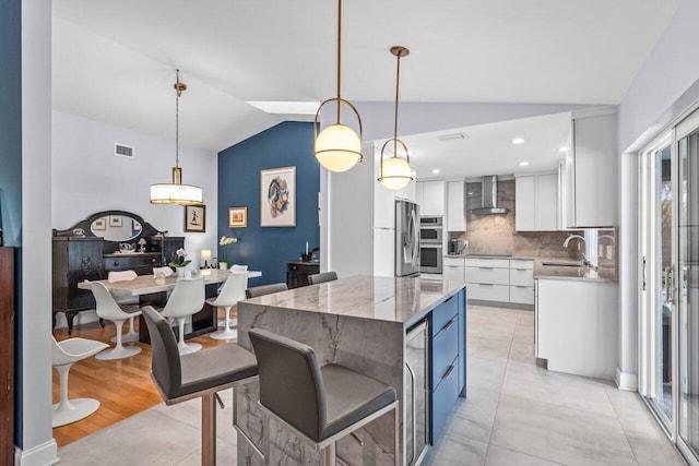 kitchen featuring sink, white cabinetry, a kitchen island, decorative light fixtures, and wall chimney exhaust hood