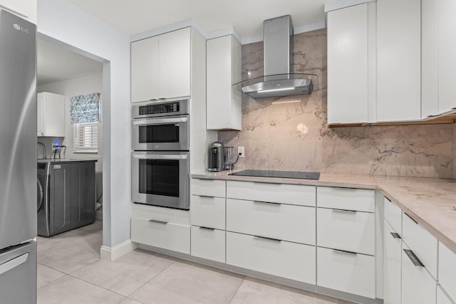 kitchen with white cabinets, decorative backsplash, light tile patterned floors, stainless steel appliances, and wall chimney exhaust hood