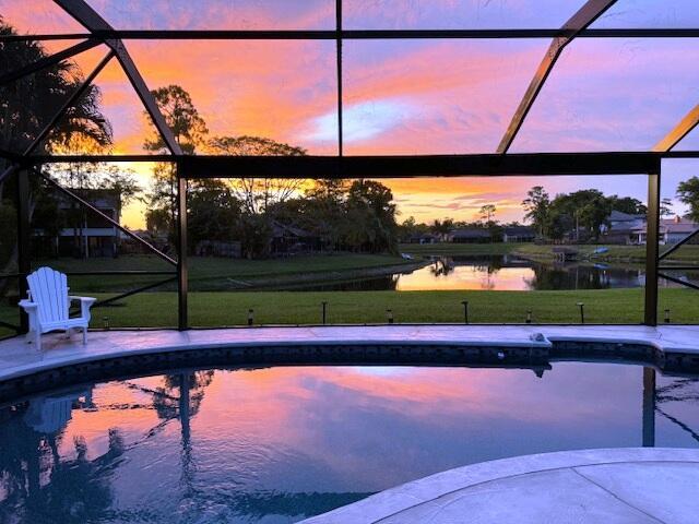 pool at dusk featuring a water view, a yard, and glass enclosure