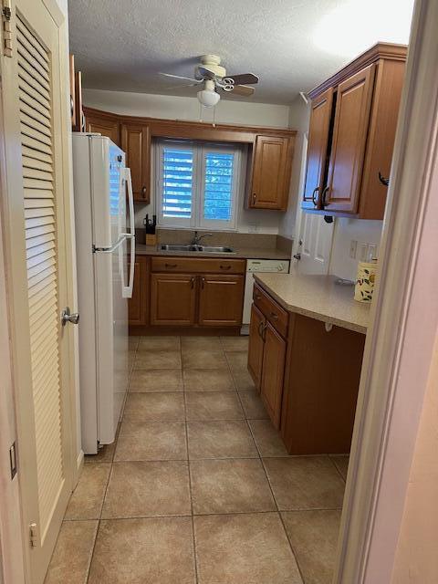 kitchen with sink, white appliances, light tile patterned floors, ceiling fan, and a textured ceiling