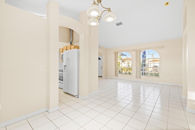 unfurnished living room with high vaulted ceiling, light tile patterned floors, and a chandelier