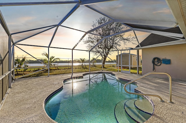 pool at dusk featuring a storage unit, a lanai, and a patio area