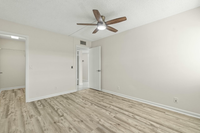 unfurnished bedroom with light hardwood / wood-style flooring, a walk in closet, ceiling fan, a textured ceiling, and a closet