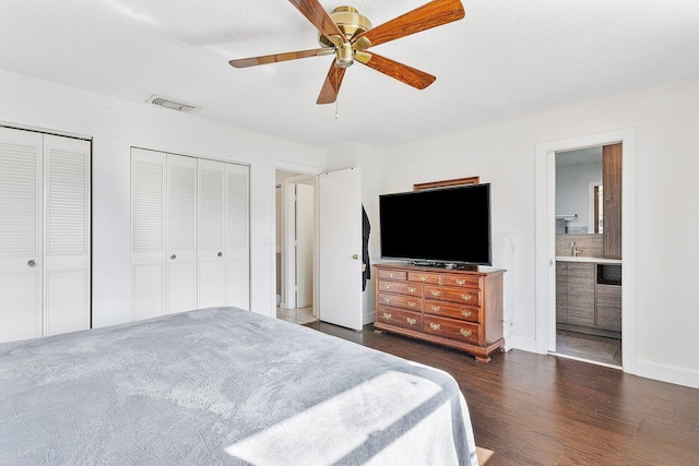 bedroom with sink, ensuite bath, dark hardwood / wood-style flooring, two closets, and ceiling fan