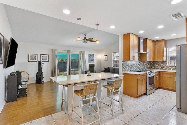 kitchen featuring appliances with stainless steel finishes, decorative light fixtures, a breakfast bar area, light tile patterned floors, and wall chimney exhaust hood