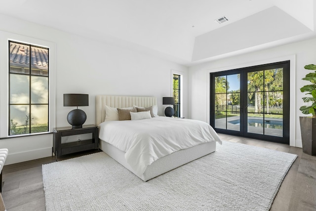 bedroom with hardwood / wood-style flooring, a raised ceiling, access to outside, and french doors