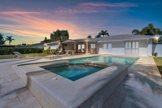 pool at dusk with an in ground hot tub and a patio