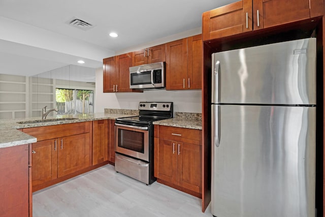 kitchen featuring sink, light stone counters, kitchen peninsula, stainless steel appliances, and light wood-type flooring