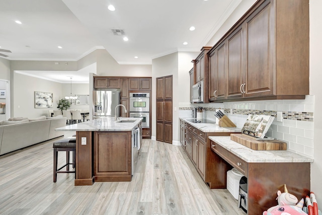 kitchen featuring a breakfast bar area, light wood-type flooring, stainless steel appliances, light stone countertops, and a kitchen island with sink