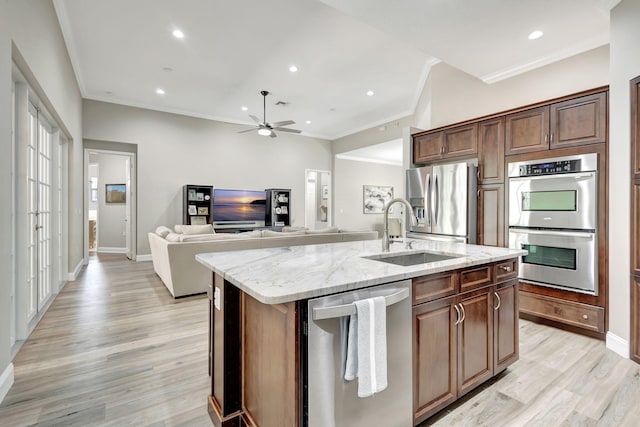 kitchen with appliances with stainless steel finishes, sink, light stone counters, crown molding, and a center island with sink