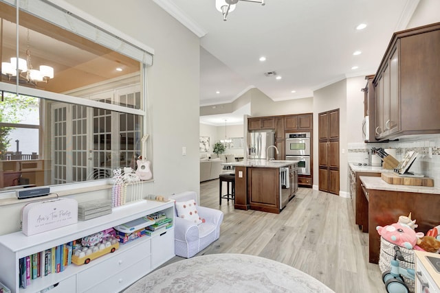 kitchen featuring appliances with stainless steel finishes, a kitchen island with sink, hanging light fixtures, a kitchen bar, and a chandelier