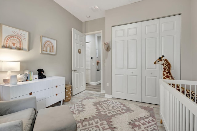 bedroom featuring a crib, light wood-type flooring, and a closet