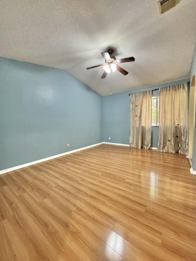 unfurnished room with light wood-type flooring, vaulted ceiling, ceiling fan, and a textured ceiling