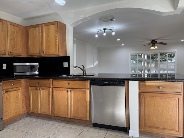 kitchen with sink, dark stone countertops, light tile patterned floors, appliances with stainless steel finishes, and ceiling fan