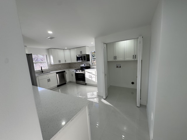 kitchen featuring white cabinetry, tasteful backsplash, light stone counters, light tile patterned floors, and appliances with stainless steel finishes