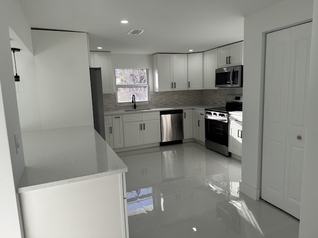 kitchen featuring appliances with stainless steel finishes, sink, white cabinets, backsplash, and light stone countertops