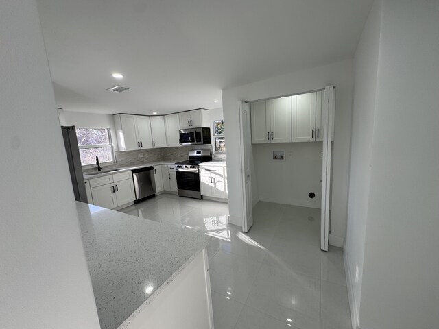 kitchen featuring tasteful backsplash, white cabinets, stainless steel fridge, hanging light fixtures, and light stone countertops