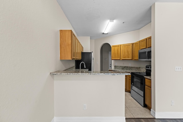 kitchen with light tile patterned flooring, sink, light stone counters, kitchen peninsula, and stainless steel appliances