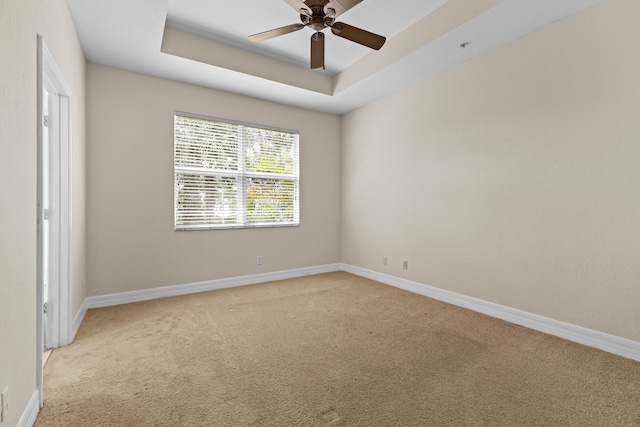 carpeted spare room featuring a raised ceiling and ceiling fan