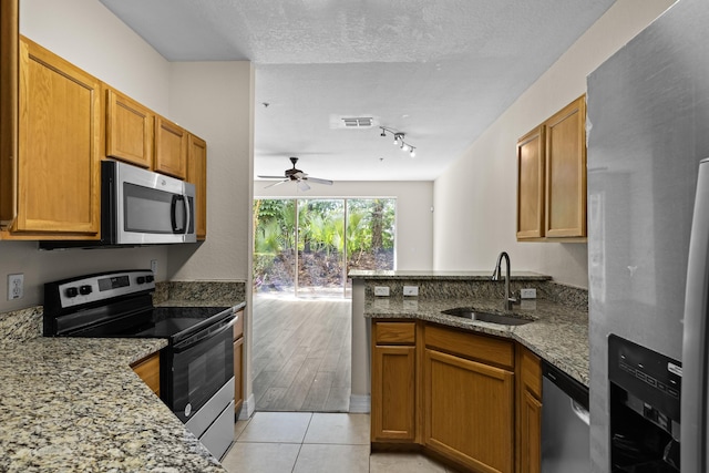 kitchen with sink, stone counters, stainless steel appliances, light tile patterned flooring, and kitchen peninsula