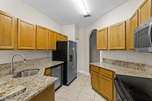 kitchen with sink, stainless steel appliances, light stone counters, a textured ceiling, and light tile patterned flooring