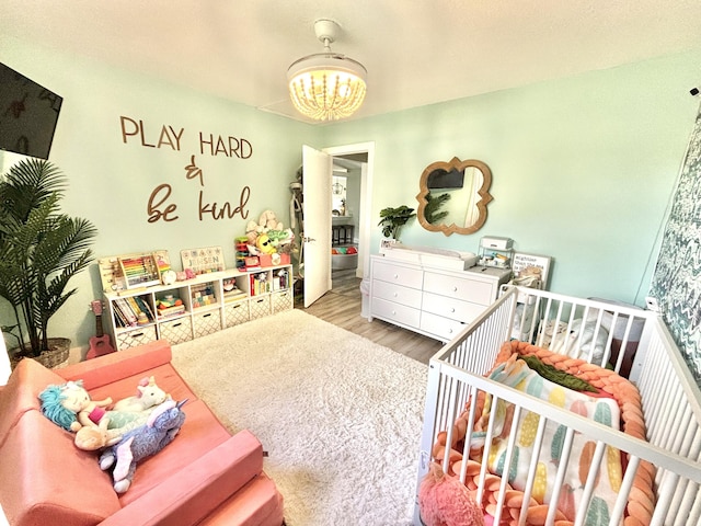 bedroom with a crib, a chandelier, and light hardwood / wood-style floors