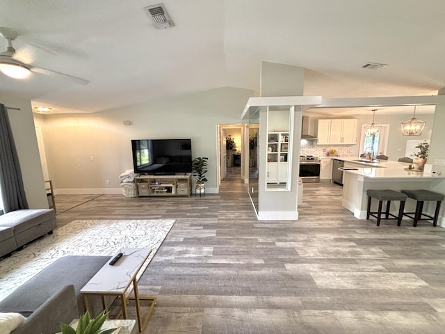 living room with lofted ceiling, sink, ceiling fan with notable chandelier, and light hardwood / wood-style floors