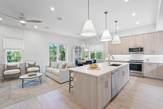 kitchen featuring a center island with sink, a sink, open floor plan, stainless steel appliances, and a decorative wall