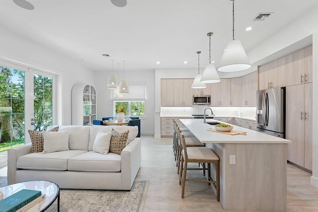 kitchen with light brown cabinetry, open floor plan, stainless steel appliances, and light countertops