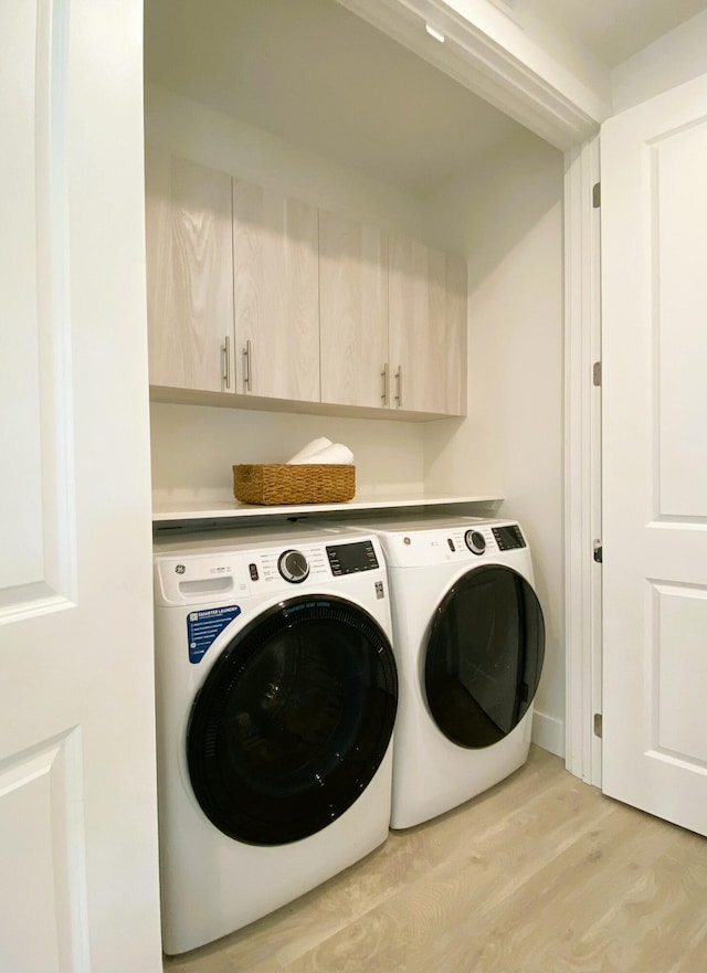 laundry area featuring washer and dryer, cabinet space, and light wood-type flooring