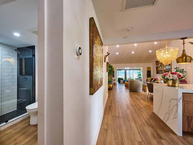 hall featuring lofted ceiling, light hardwood / wood-style floors, and a notable chandelier