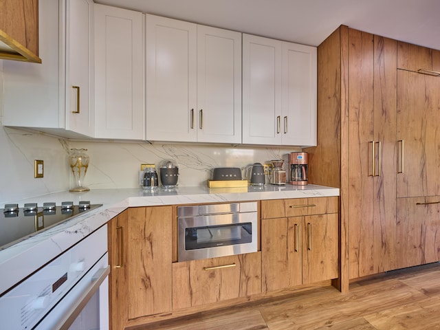 kitchen with white cabinets, decorative backsplash, light hardwood / wood-style floors, white oven, and black electric cooktop