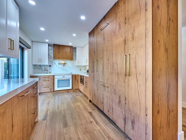 kitchen with white cabinetry, light hardwood / wood-style floors, white oven, and backsplash